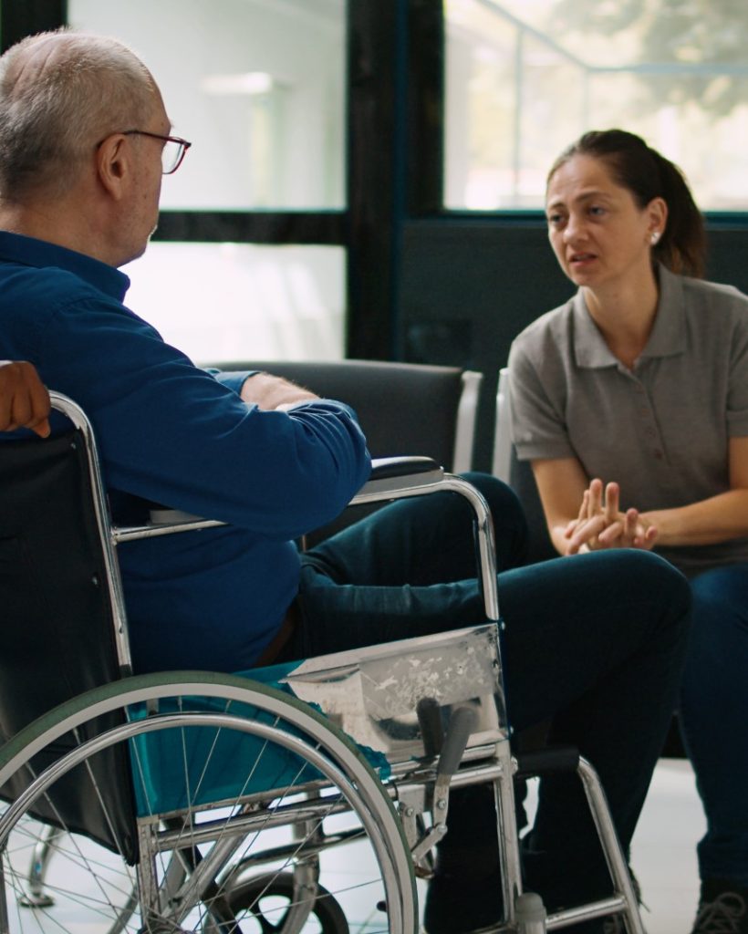 nurse-helping-man-wheelchair-meet-with-family-clinic-lobby-old-patient-dealing-with-chronic-impairment-facility-mother-child-visiting-senior-person-waiting-room (Large)